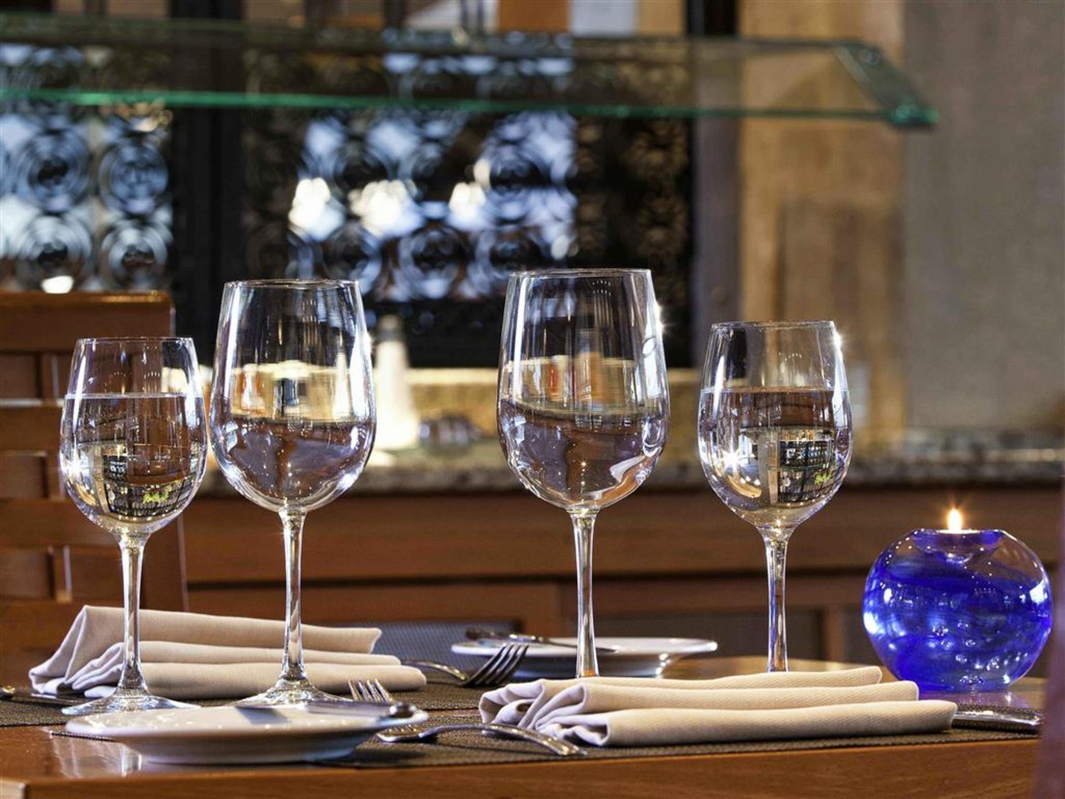 Sofitel Athens Airport Hotel Spata  Bagian luar foto The photo shows a dining table set with four elegant wine glasses filled with water. The glasses are positioned in a row on the table. Next to each glass, there are neatly folded napkins and forks. There is also a small blue decorative candle holder 