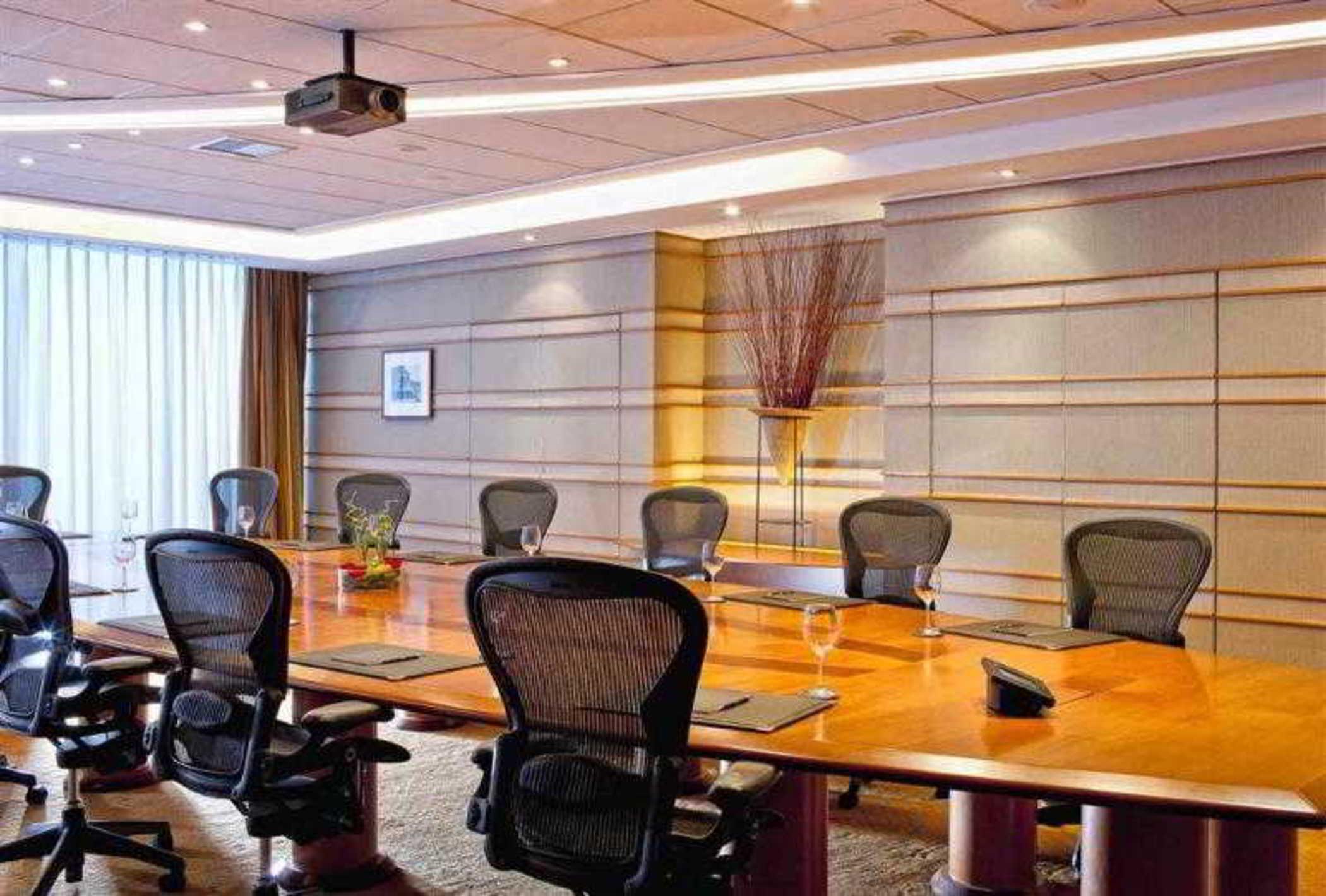Sofitel Athens Airport Hotel Spata  Bagian luar foto The photo shows a modern conference room. It features a long wooden table surrounded by ergonomic office chairs. The room is well-lit with recessed lighting and has a projector hanging from the ceiling. Large windows allow natural light to enter, wit