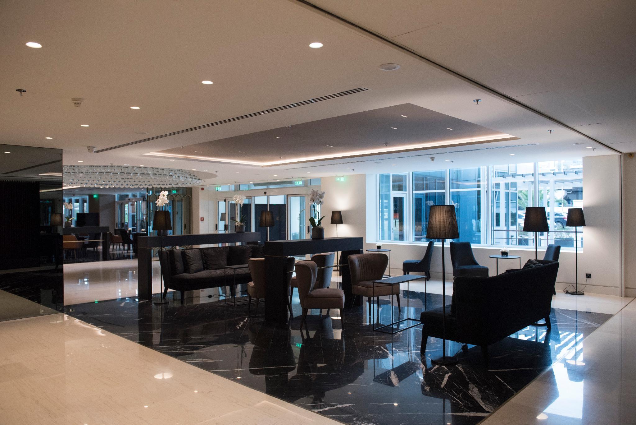Sofitel Athens Airport Hotel Spata  Bagian luar foto The photo shows a modern lobby or lounge area. It features sleek, contemporary furniture including black leather sofas and chairs, paired with elegant tables. The flooring appears to be dark marble, adding a touch of luxury. The space is well-lit wit