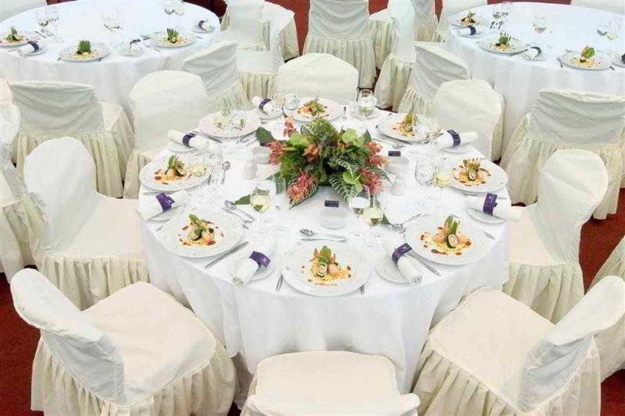 Sofitel Athens Airport Hotel Spata  Bagian luar foto The image shows a beautifully arranged dining setup. There are several round tables covered with white tablecloths, and each table is surrounded by white chairs, likely dressed in covers that drape to the ground. 

On each table, there are elegant pl