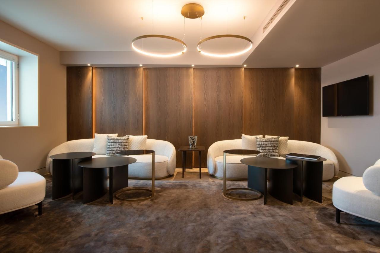 Sofitel Athens Airport Hotel Spata  Bagian luar foto The photo shows a modern and stylish interior space designed for relaxation or social gatherings. It features two curved white sofas positioned around small, round black tables. The walls are adorned with dark wooden panels, providing a warm contrast