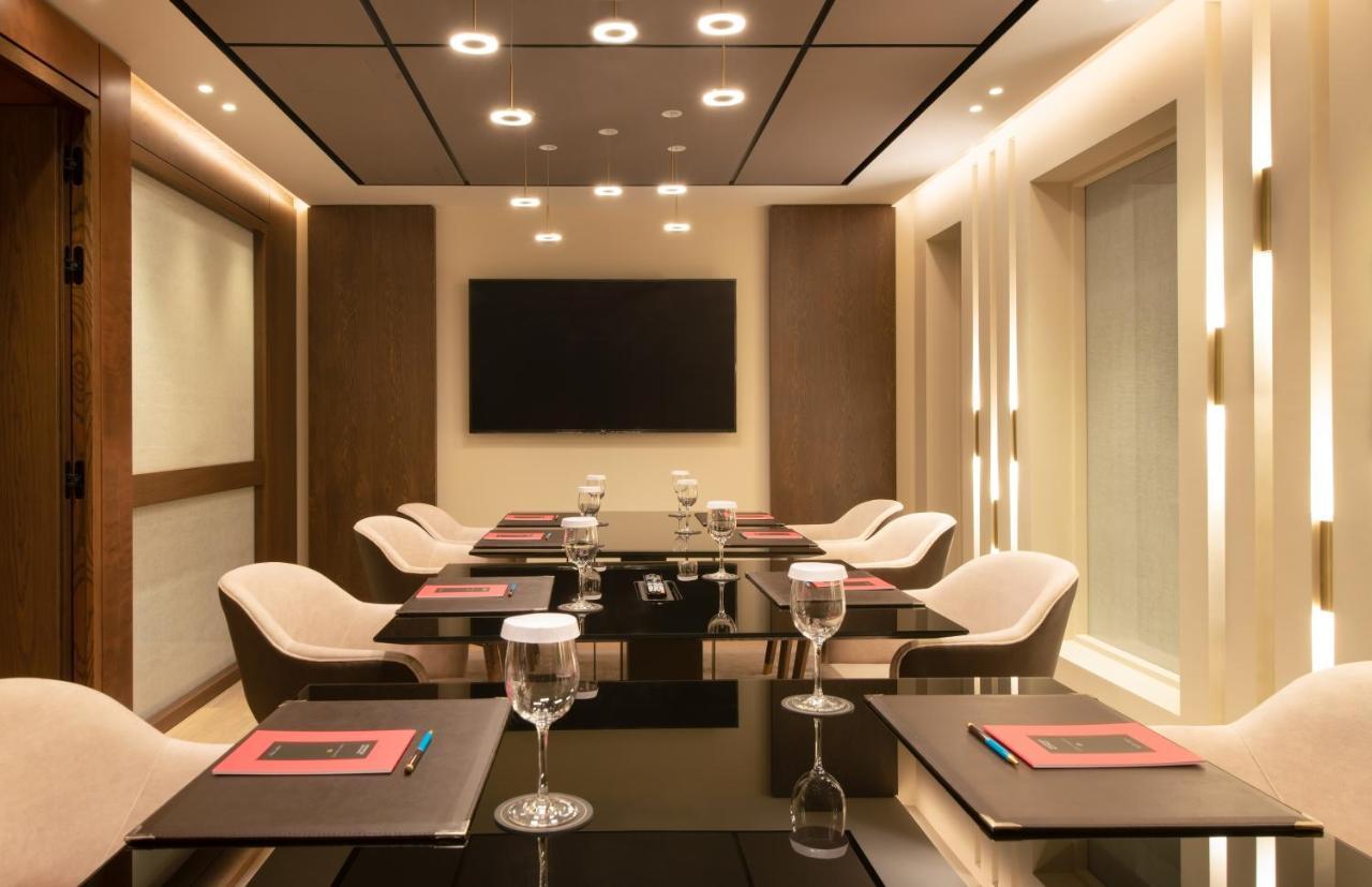 Sofitel Athens Airport Hotel Spata  Bagian luar foto The photo depicts a modern conference room. It features a sleek glass table surrounded by stylish chairs. Each place setting includes a glass of water and a menu or notepad. The room is well-lit with recessed lighting and has a large flat-screen tele
