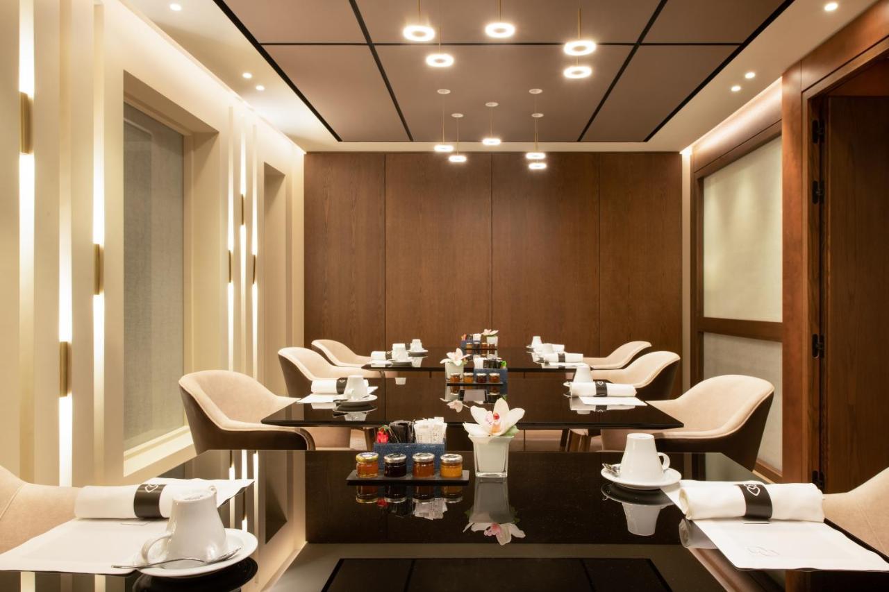 Sofitel Athens Airport Hotel Spata  Bagian luar foto The photo shows a modern and elegantly designed dining or meeting room. It features a sleek, dark table surrounded by several light-colored chairs. The walls are adorned with warm wood paneling, and the ceiling has recessed lighting that adds a soft 