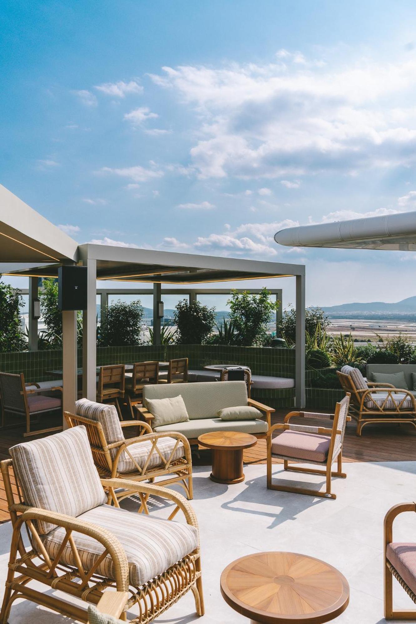 Sofitel Athens Airport Hotel Spata  Bagian luar foto The photo depicts a stylish rooftop space designed for relaxation and socializing. It features comfortable seating arrangements, including sofas and armchairs, made from natural materials such as wood and fabric. The area is partially shaded by struc