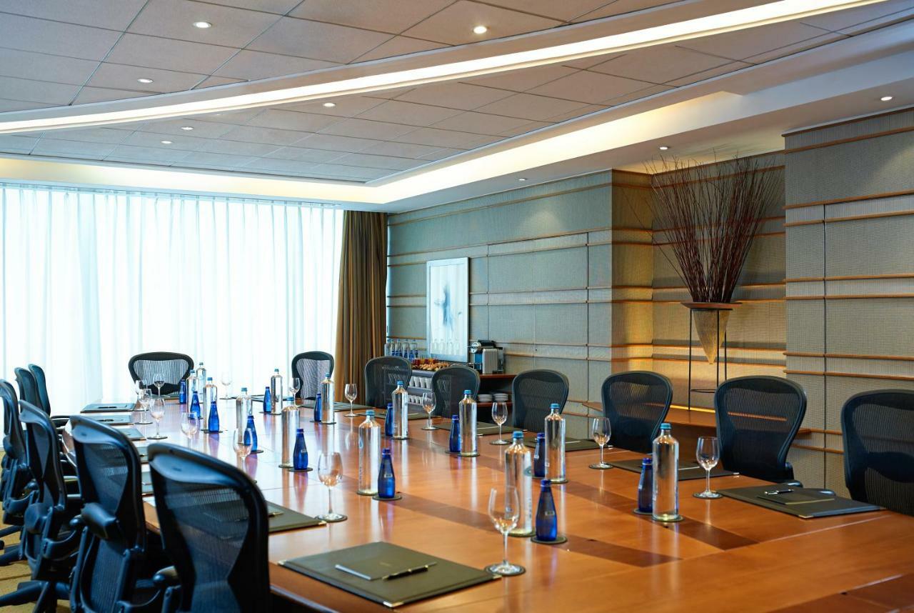 Sofitel Athens Airport Hotel Spata  Bagian luar foto The photo shows a conference room featuring a long wooden table surrounded by black ergonomic chairs. Each place at the table is set with a notepad and a pen. There are several blue glass water bottles positioned at intervals along the table, alongsi