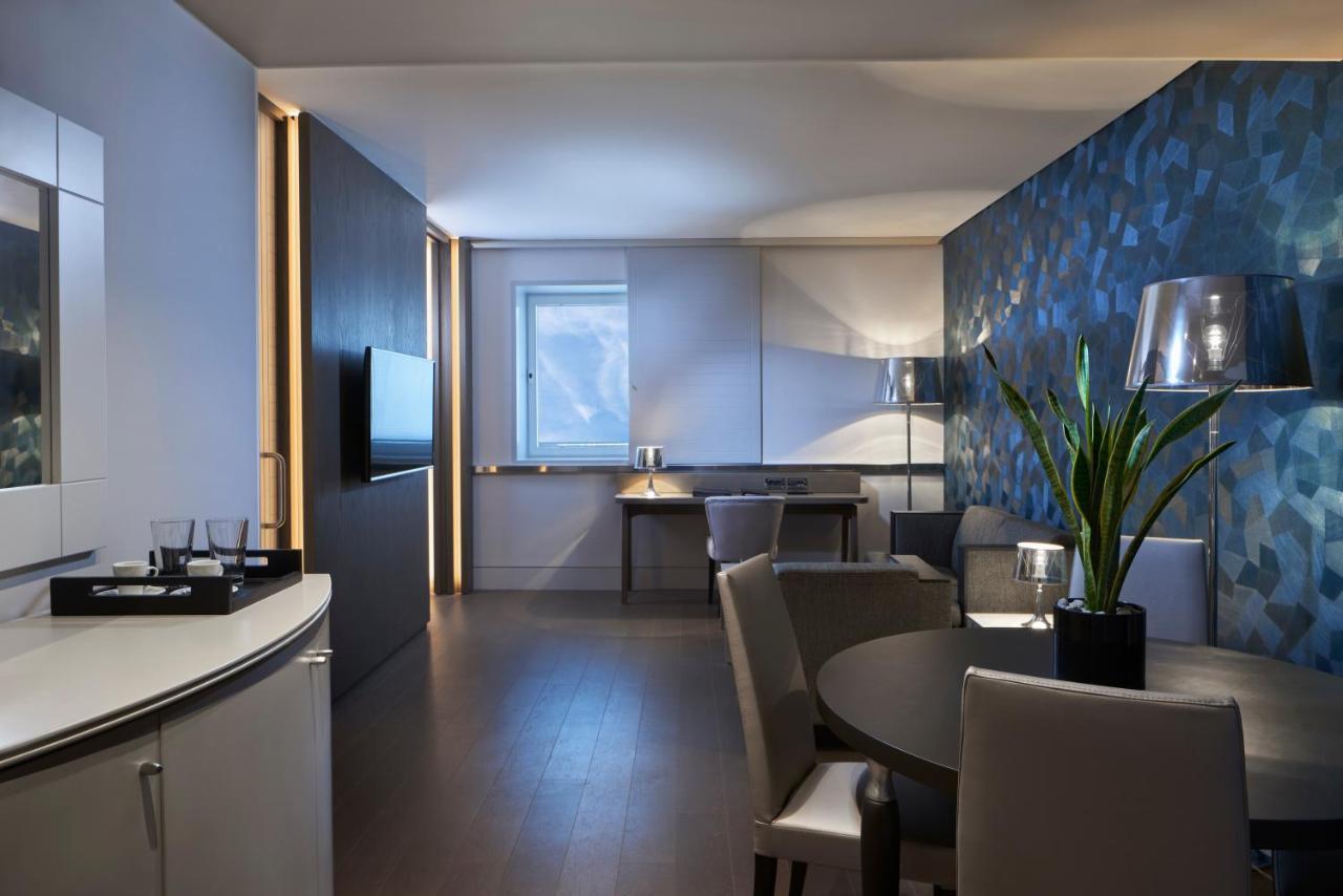 Sofitel Athens Airport Hotel Spata  Bagian luar foto The photo shows a modern living space, likely a hotel suite or an upscale apartment. The room features a stylish and minimalist design with a combination of light and dark elements. 

- **Seating Area:** There are a couple of comfortable-looking chai